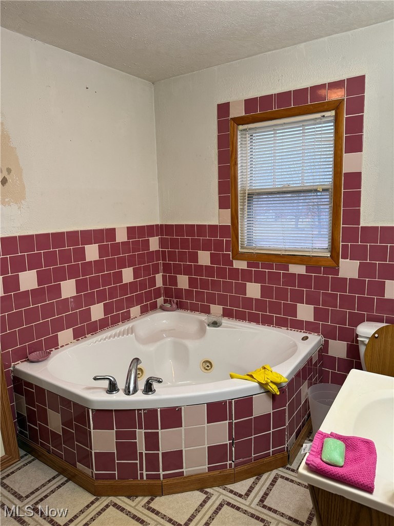 1311 Warner Road Southeast Canton, OH 44707 - Photo 7 of 14 Bathroom with a tub with jets, vanity, tile walls, and a textured ceiling