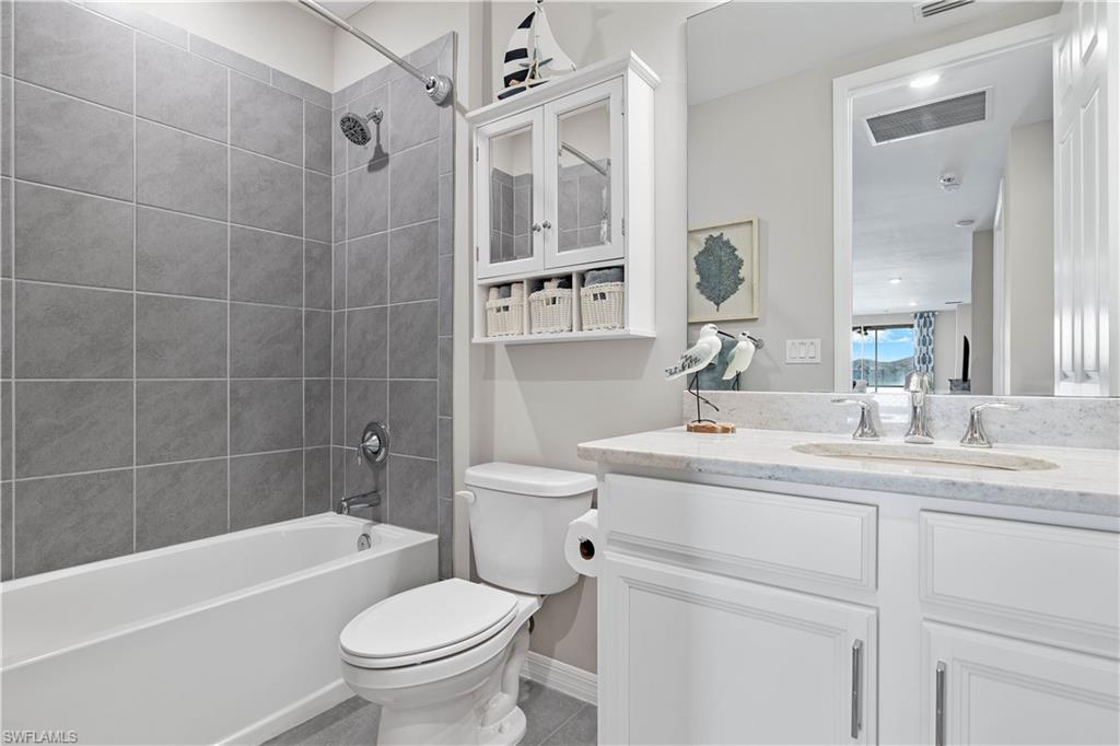 14558 Edgewater Circle Naples, FL 34114 - Photo 20 of 40 a bathroom with a granite countertop toilet a sink a mirror a bathtub and shower