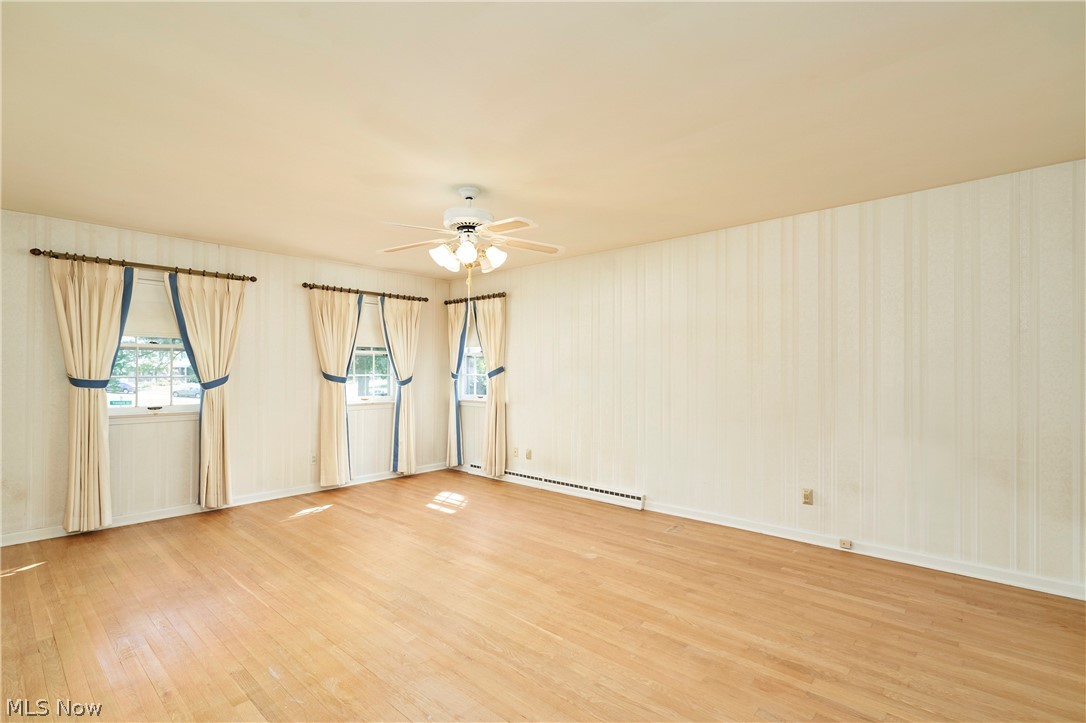 354 Tremont Road Akron, OH 44313 - Photo 20 of 34 Spacious room featuring light wood-finish flooring, three windows with curtains, a ceiling fan with integrated lighting, and textured wall coverings