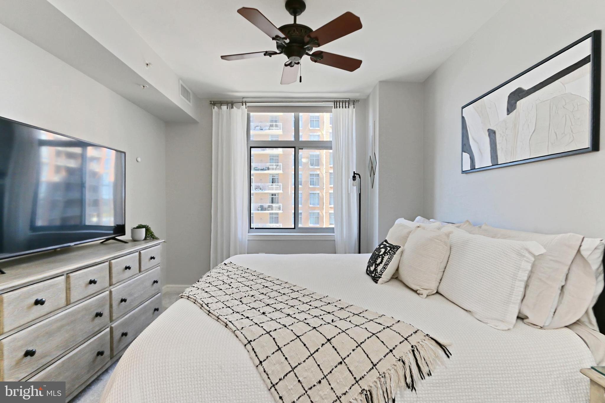 11990 Market Street, Unit 908 Reston, VA 20190 - Photo 14 of 45 a bedroom with a large bed and a flat tv screen on dresser