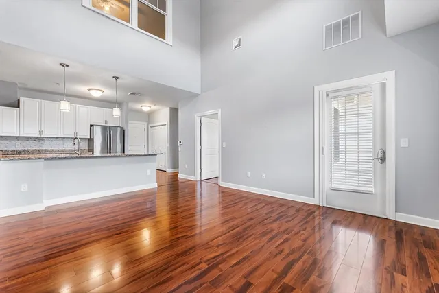 a view of an empty room with wooden floor and a kitchen