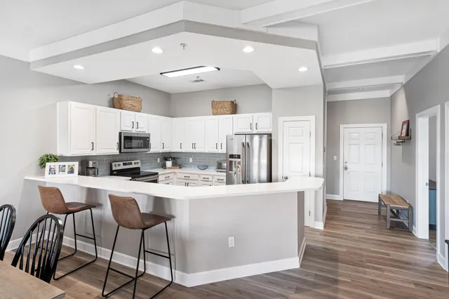 a kitchen with stainless steel appliances a refrigerator a stove a sink a dining table and chairs with wooden floor