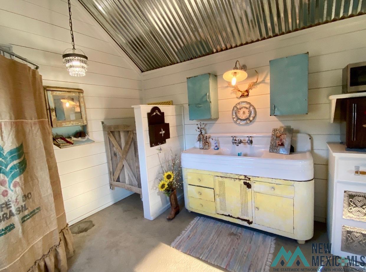 1131 Curry Road North Clovis, NM 88101 - Photo 52 of 69 Corrugated metal ceiling with exposed beams, white shiplap walls, a large porcelain double-basin sink with a yellow base cabinet, two blue wall-mounted cabinets, and concrete flooring