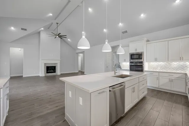a kitchen with a stove a sink a microwave and white cabinets with wooden floor