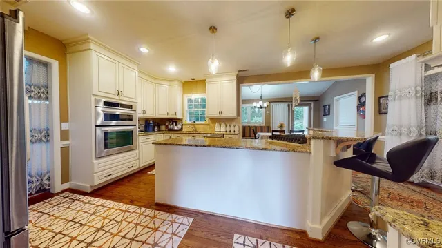 a open kitchen with stainless steel appliances granite countertop a refrigerator a oven a stove and a sink with wooden floor