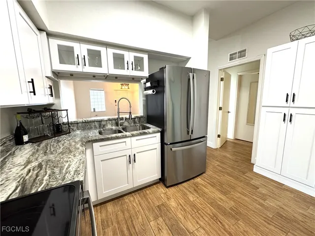 a kitchen with stainless steel appliances granite countertop a refrigerator a stove a sink and white cabinets with wooden floor