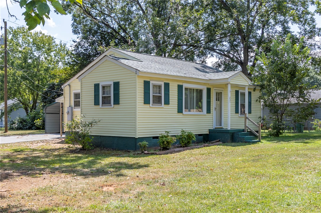 Mature trees frame a charming classic cottage featuring a neat lawn and custom shutters.