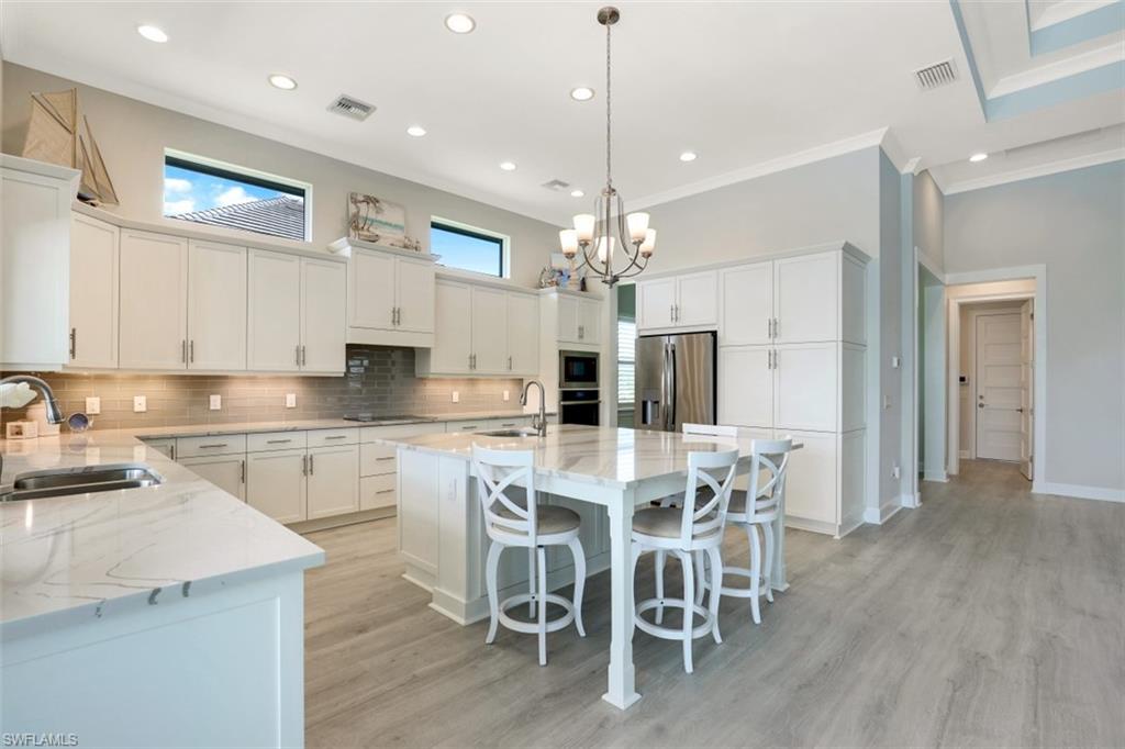 5771 Clarendon Drive Naples, FL 34113 - Photo 7 of 33 a large kitchen with kitchen island a dining table chairs and white cabinets