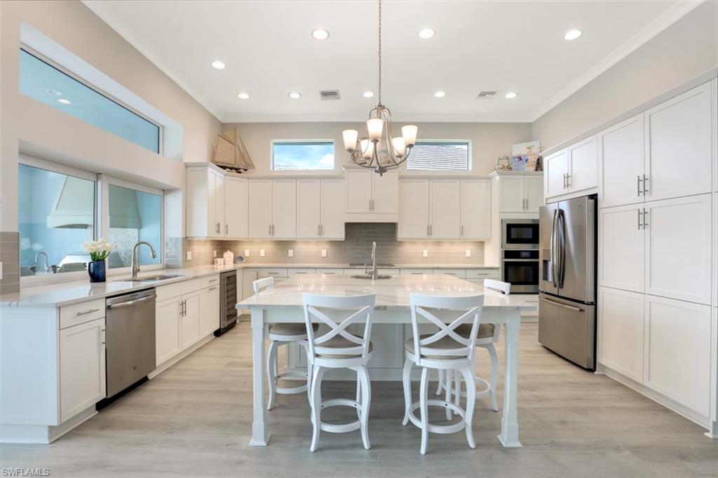 5771 Clarendon Drive Naples, FL 34113 - Photo 8 of 33 a kitchen with kitchen island granite countertop stainless steel appliances lots of white cabinets a dining table and chairs