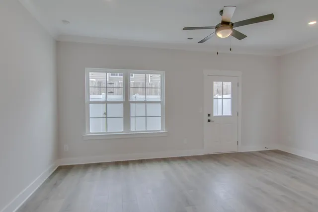 an empty room with wooden floor ceiling fan and windows