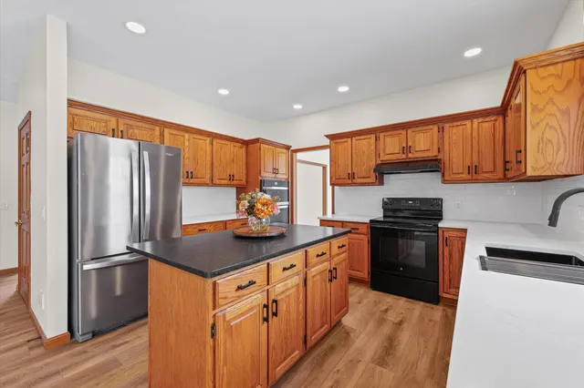 a kitchen with stainless steel appliances granite countertop a refrigerator a sink dishwasher and a oven with wooden floor