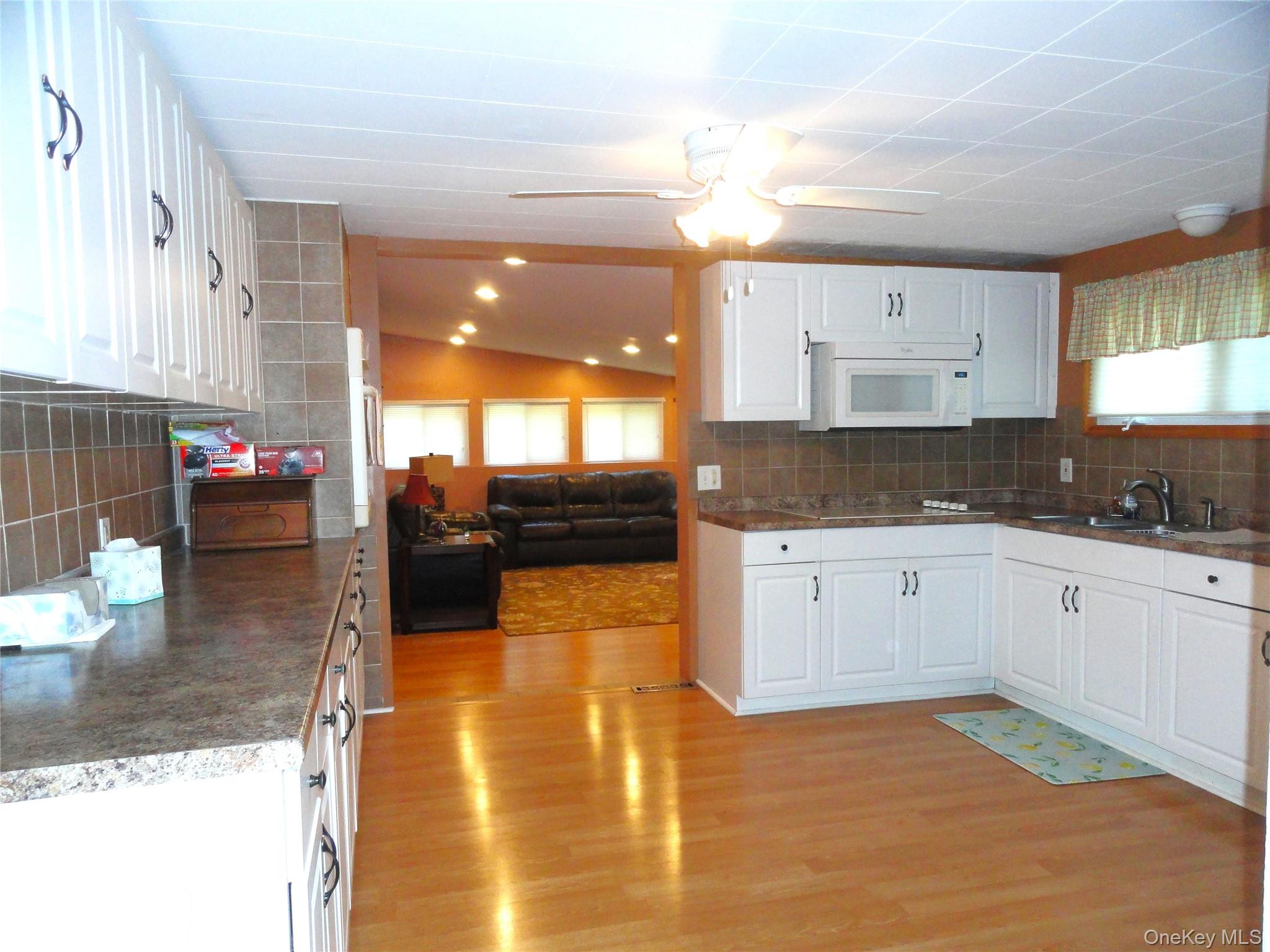 198 Tinkertown Road Salt Point, NY 12578 - Photo 8 of 25 Kitchen featuring laminate floors, white cabinetry, backsplash, built-in microwave, and lofted ceiling