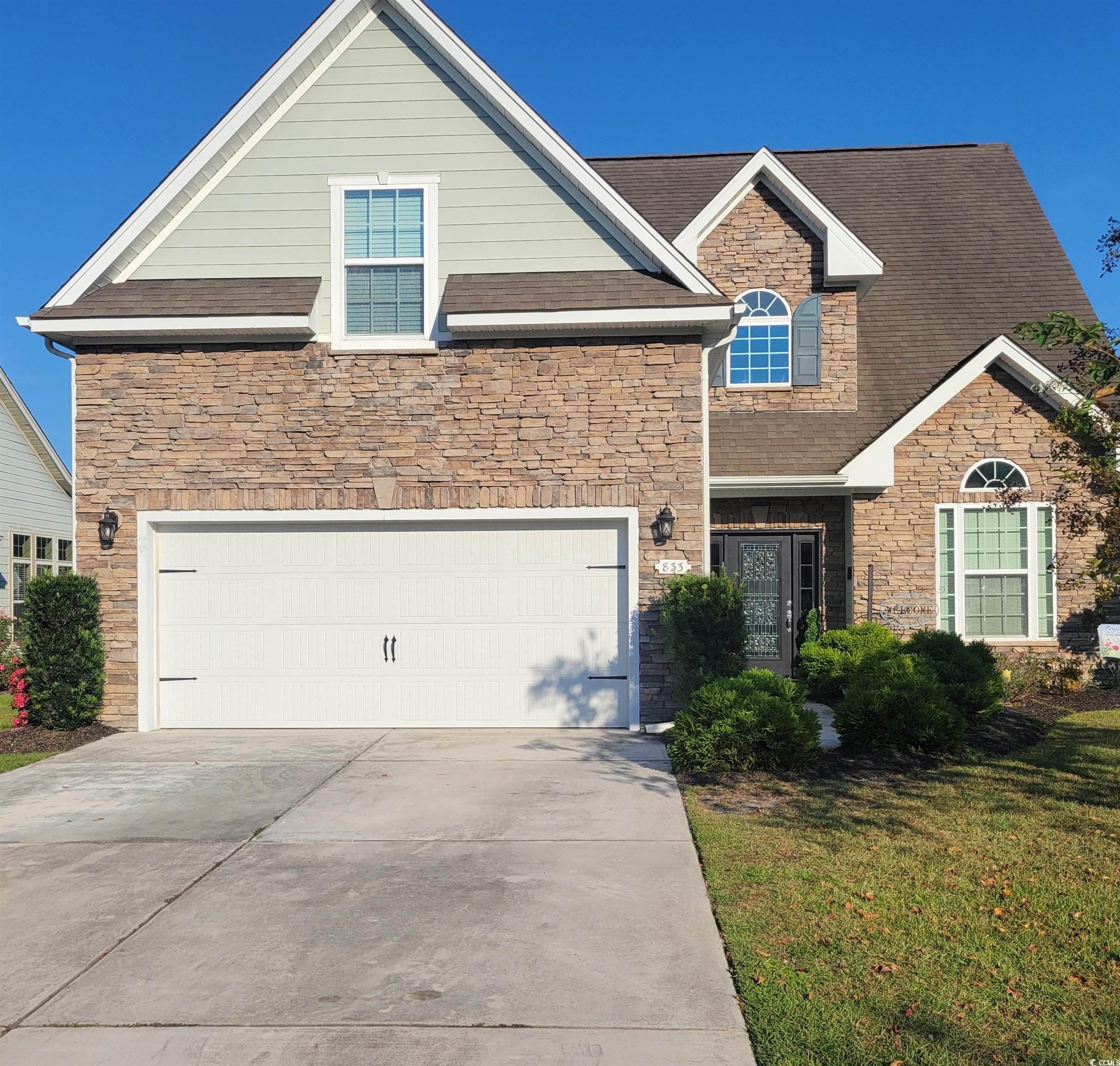 View of front of home featuring stone siding, concrete driveway, and a shingled roof