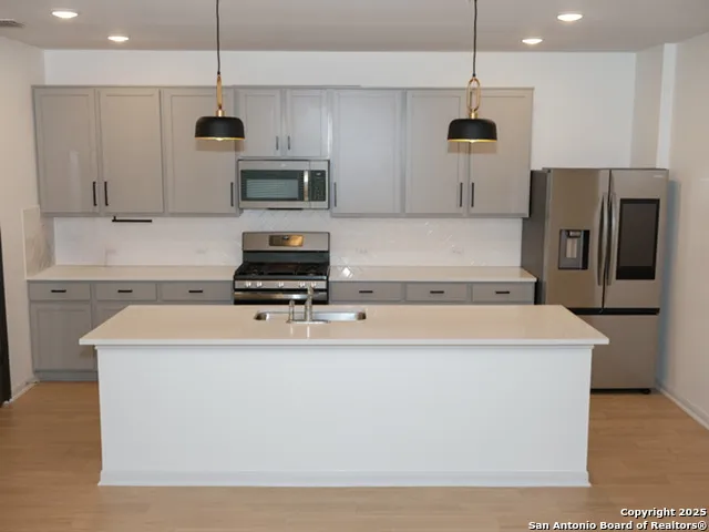 a view of kitchen with kitchen island stainless steel appliances a sink and wooden floor