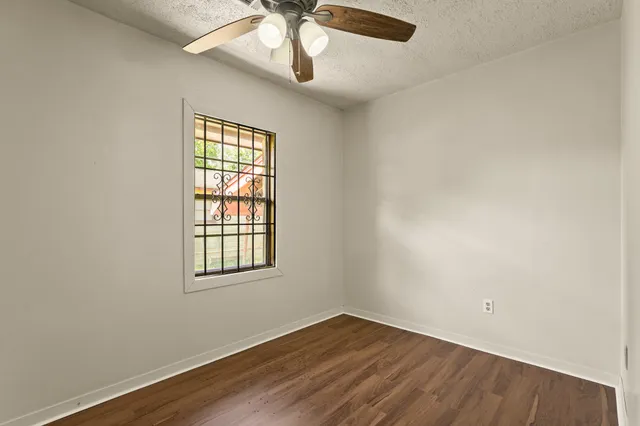 an empty room with wooden floor chandelier fan and windows