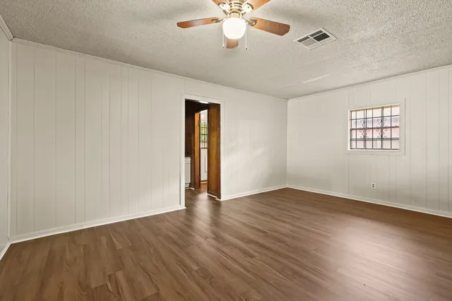 an empty room with wooden floor chandelier fan and windows