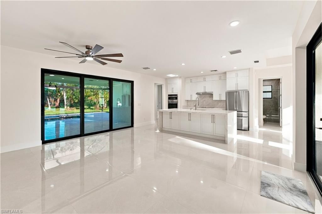 Spacious interior with large format tile flooring, modern kitchen featuring white cabinetry and stainless steel appliances, and expansive sliding glass doors