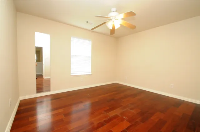 an empty room with wooden floor fan and window