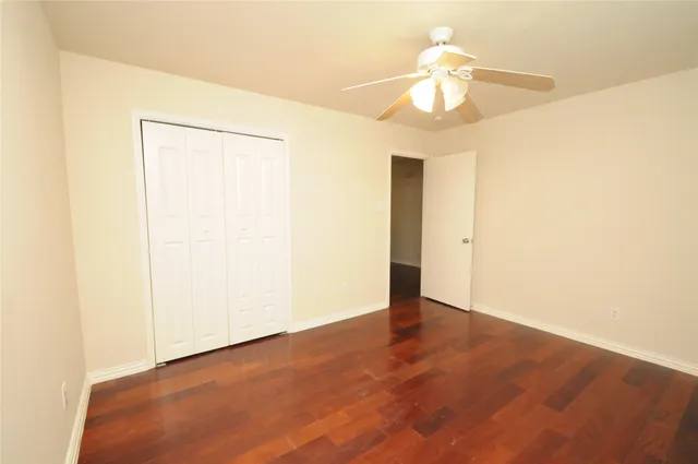 an empty room with a chandelier fan and wooden floor
