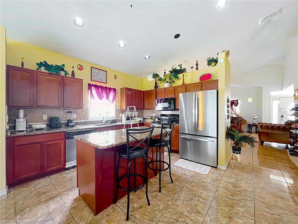 7939 Riffle Lane Orlando, FL 32818 - Photo 13 of 52 a kitchen with stainless steel appliances kitchen island granite countertop a table chairs stove and refrigerator
