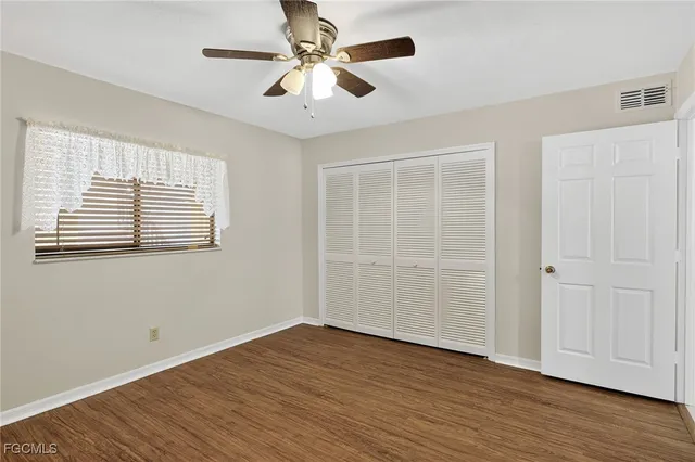 an empty room with wooden floor chandelier fan and windows