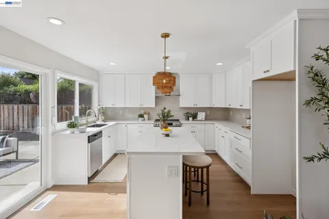 a kitchen with a stove a sink a kitchen island with chairs and wooden floor