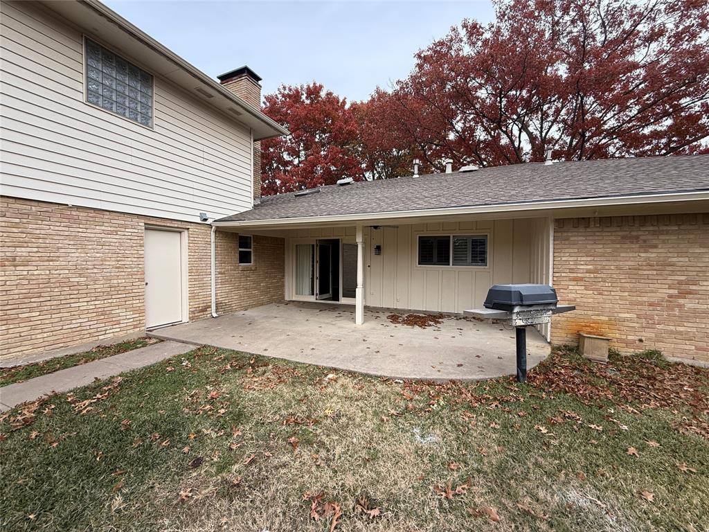 4916 Sugar Mill Road Dallas, TX 75244 - Photo 17 of 18 Property entrance featuring a patio area, roof with shingles, a yard, a chimney, and brick siding
