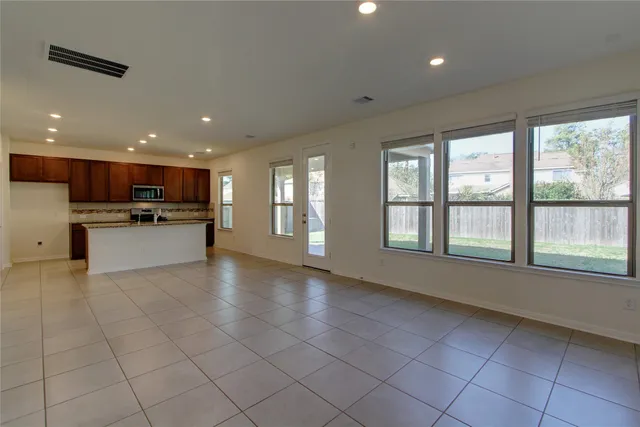 a view of an empty room with kitchen and window