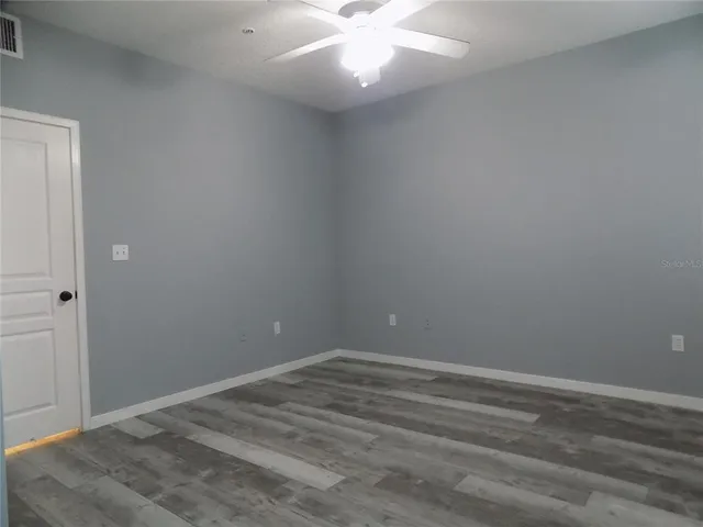 a view of an empty room with wooden floor and ceiling fan