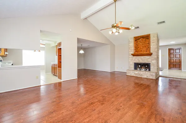 a view of an empty room with wooden floor and a kitchen