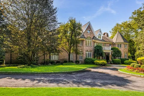 a view of a big house with a big yard and potted plants and large trees