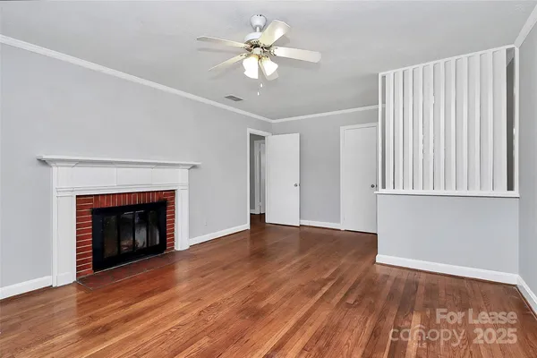 a view of an empty room with wooden floor fireplace and a window