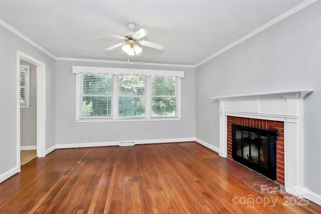 a view of an empty room with wooden floor fireplace and a window