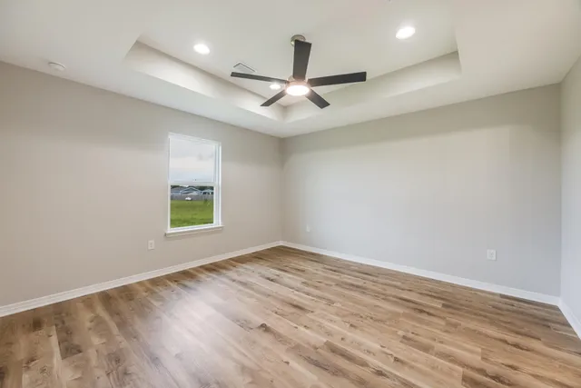 an empty room with wooden floor ceiling fan and windows