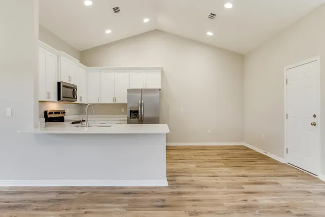 a view of kitchen with stainless steel appliances granite countertop a stove top oven a sink dishwasher and a refrigerator with wooden floor