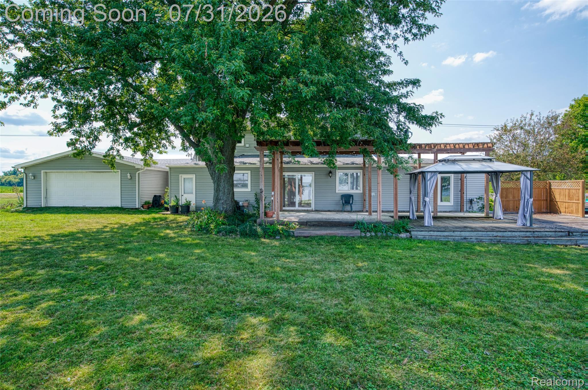 5269 Reno Road Manchester, MI 48158 - Photo 27 of 64 Expansive rear yard featuring a large wooden deck with a pergola, a detached two-car garage, and a mature tree providing shade
