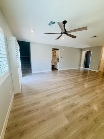 a view of an empty room with wooden floor and a ceiling fan