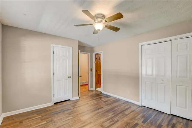 an empty room with wooden floor chandelier fan and windows