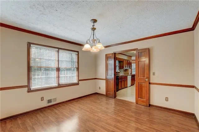 an empty room with wooden floor chandelier and windows