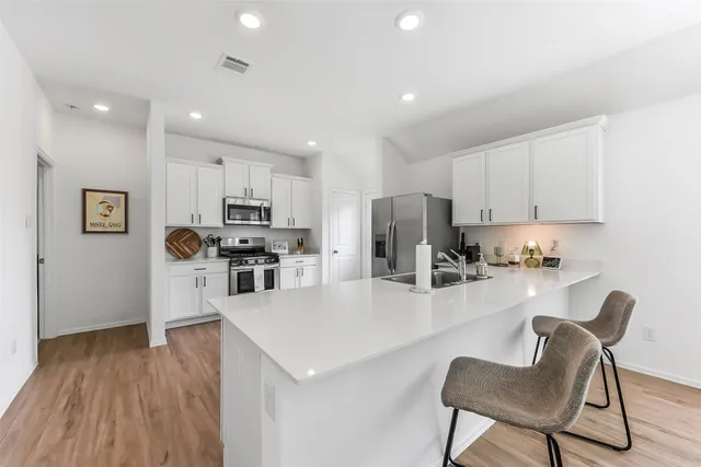 a kitchen with a refrigerator a stove a sink a dining table and chairs with wooden floor