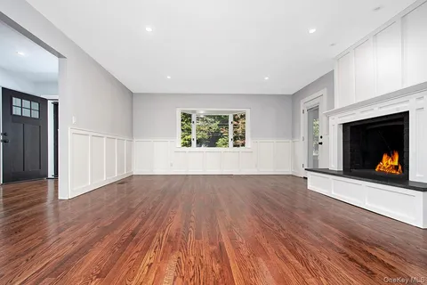 a view of an empty room with wooden floor fireplace and a window