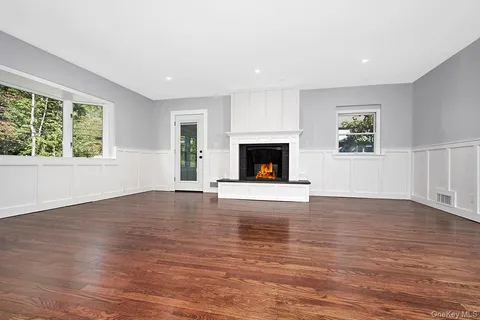 a view of an empty room with wooden floor fireplace and a window