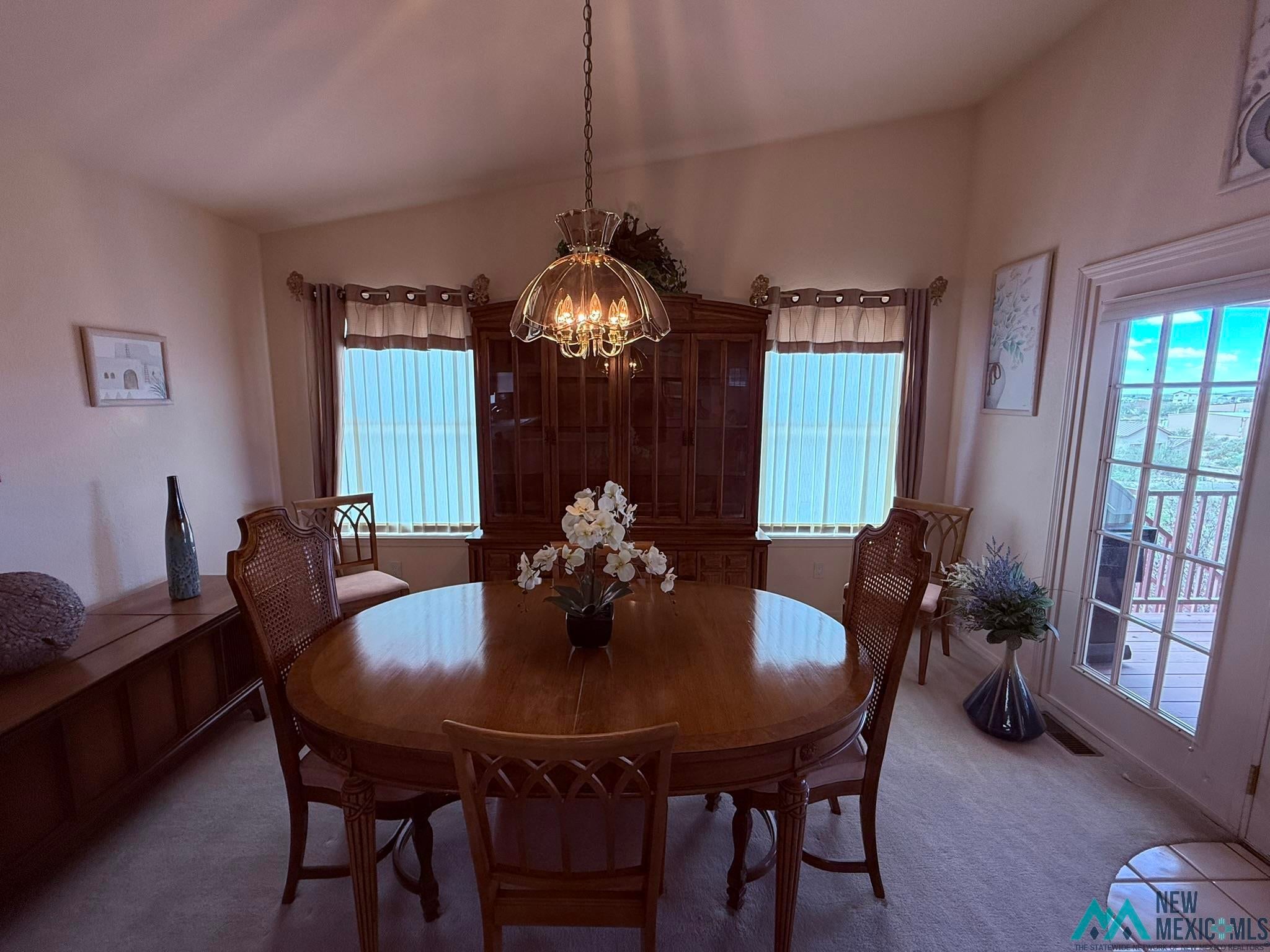300 Rio Grande Circle Elephant Butte, NM 87935 - Photo 56 of 99 Vaulted ceiling dining area featuring a prominent chandelier, dual windows with vertical blinds, and a glass-paned door opening to an outdoor deck
