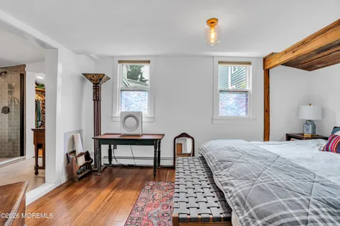 a bedroom with a bed a dresser with wooden floor and windows