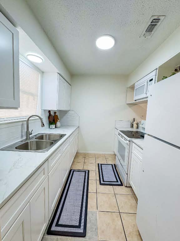 5810 Sweeney Circle, Unit D Austin, TX 78723 - Photo 6 of 18 Kitchen with white appliances, white cabinets, a textured ceiling, light tile patterned floors, and light stone counters