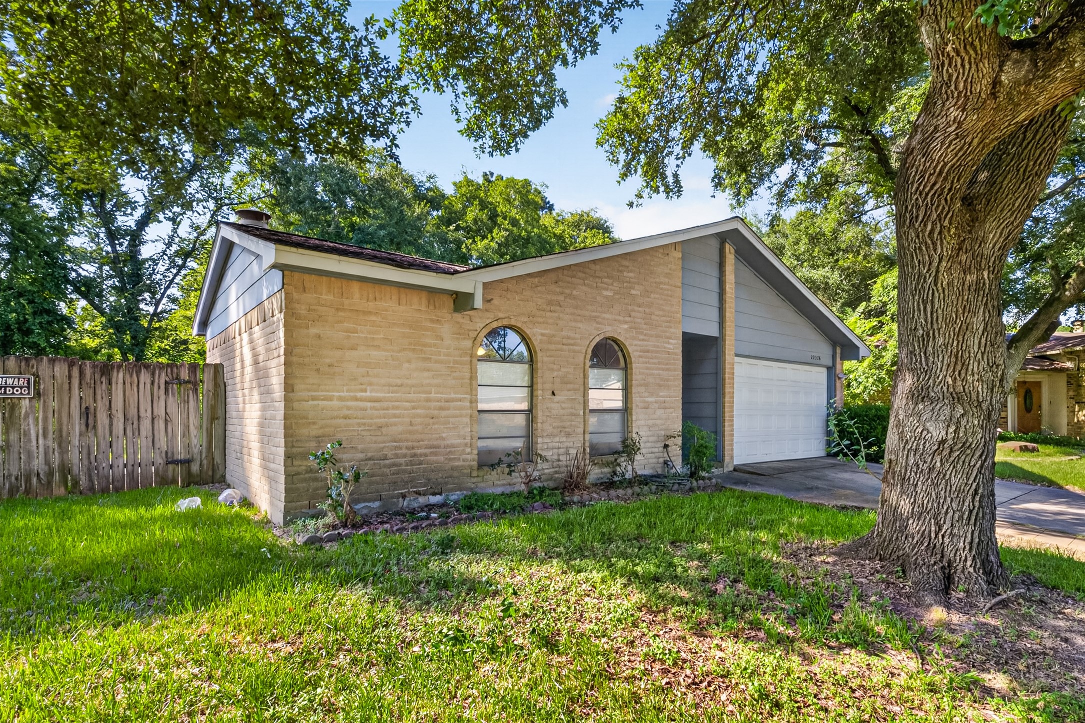 22926 Millgate Drive Spring, TX 77373 - Photo 3 of 34 This charming single-story home features a brick facade with arched windows, a two-car garage, and a lush front yard with mature trees, creating a welcoming and serene atmosphere.