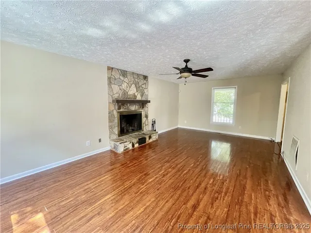 an empty room with wooden floor fireplace and windows