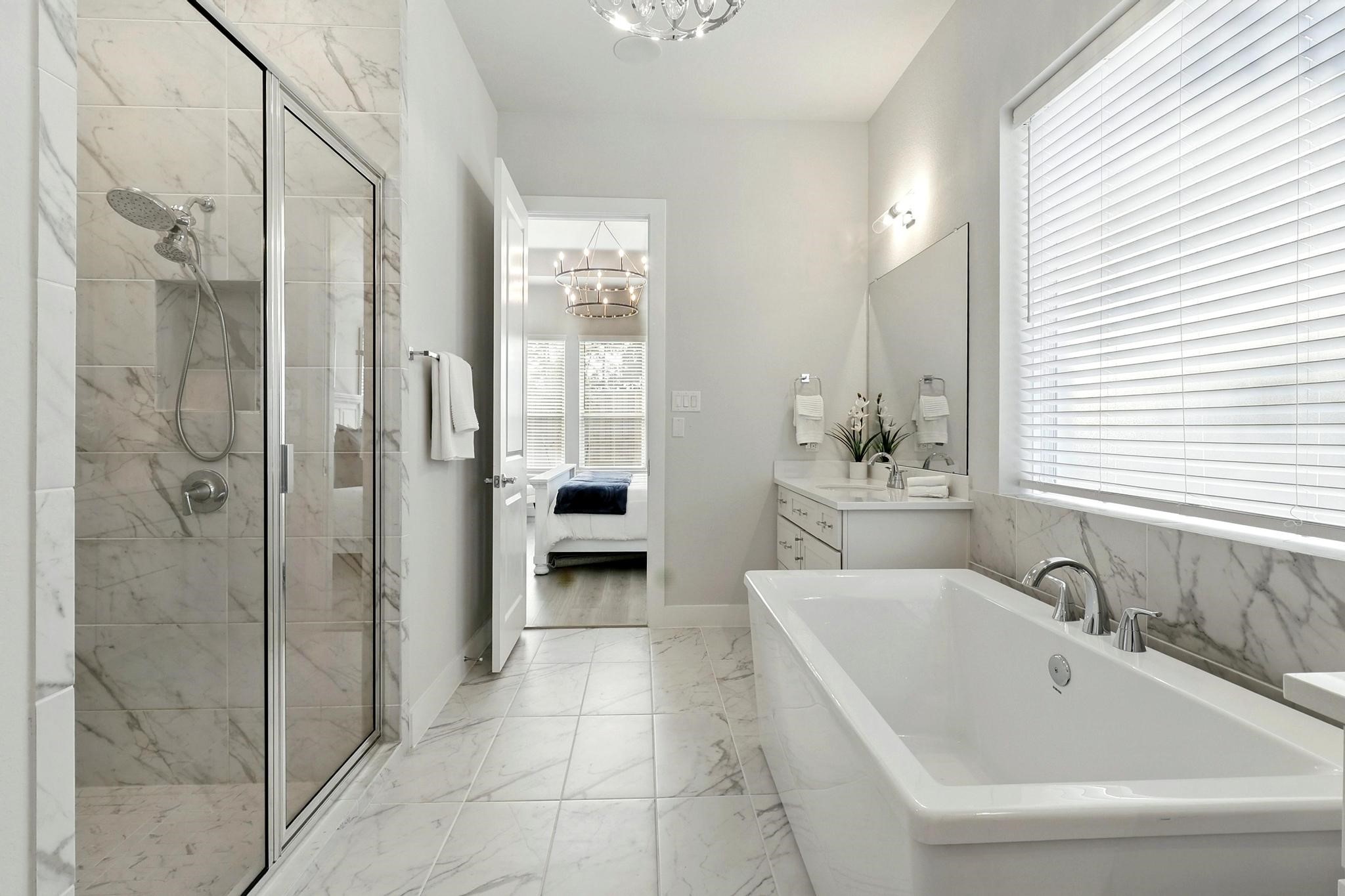26923 Arethusa Court Spring, TX 77389 - Photo 15 of 44 This elegant bathroom features a spacious walk-in shower with glass doors, a luxurious freestanding bathtub, and sleek, modern fixtures. The room is brightened by natural light from a large window with blinds, and the neutral tones create a serene atmosphere.