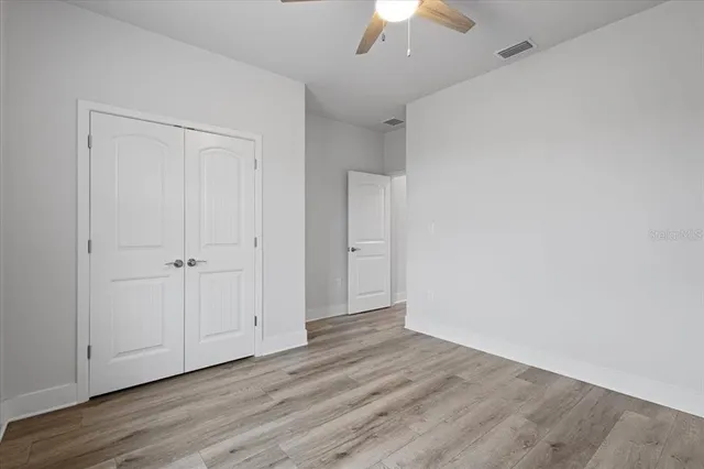 an empty room with wooden floor chandelier fan and windows