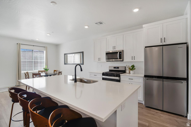 1705 Ripple Rock Drive, Unit 3017 Washington, UT 84780 - Photo 4 of 22 Contemporary kitchen featuring a large central island with a sink, white cabinetry, stainless steel appliances, and wood-finish flooring